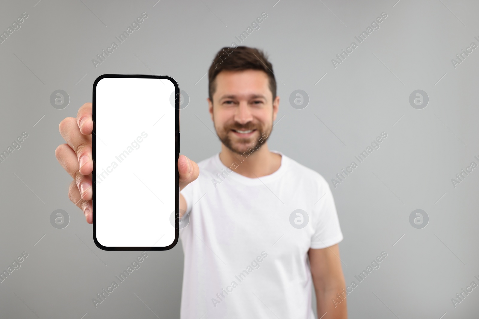 Photo of Handsome man showing smartphone in hand on light grey background, selective focus. Mockup for design