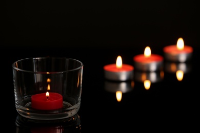 Photo of Wax candles burning on table in darkness. Space for text
