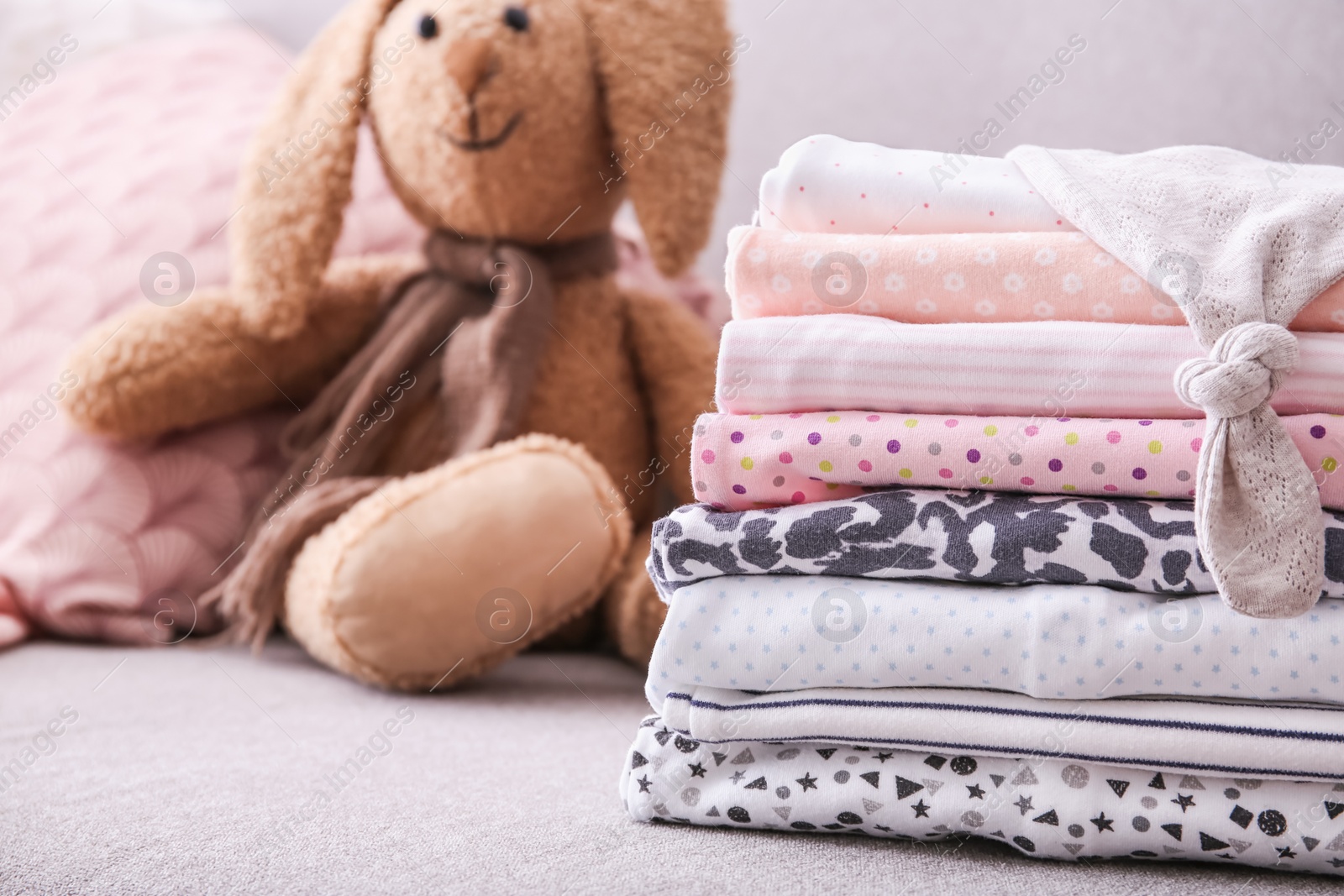 Photo of Stack of stylish child clothes and toy bunny on couch