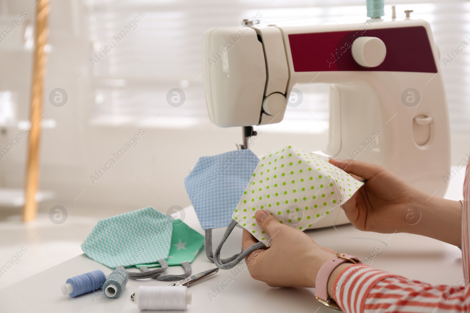 Photo of Woman making cloth mask with sewing machine at white table, closeup