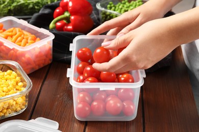 Photo of Woman putting tomatoes into plastic container at wooden table, closeup. Food storage
