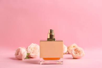 Bottle of perfume with beautiful roses on color background