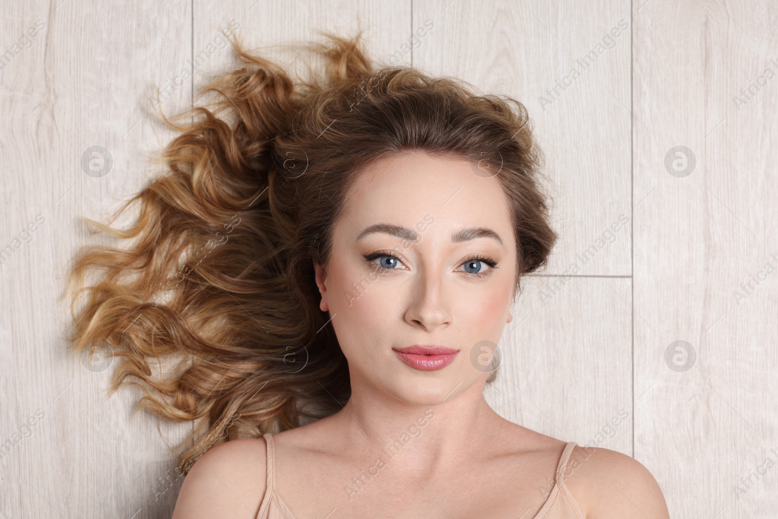 Photo of Portrait of beautiful woman with curly hair on wooden floor, top view