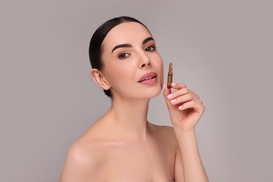 Beautiful young woman holding skincare ampoule on grey background