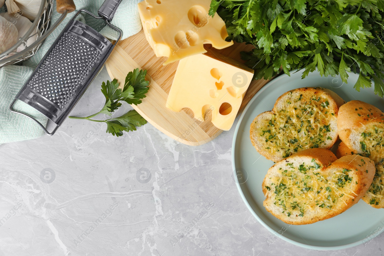 Photo of Slices of toasted bread with garlic, cheese and herbs on grey table, flat lay. Space for text