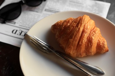 Photo of Tasty croissant, newspaper and sunglasses on black table, closeup