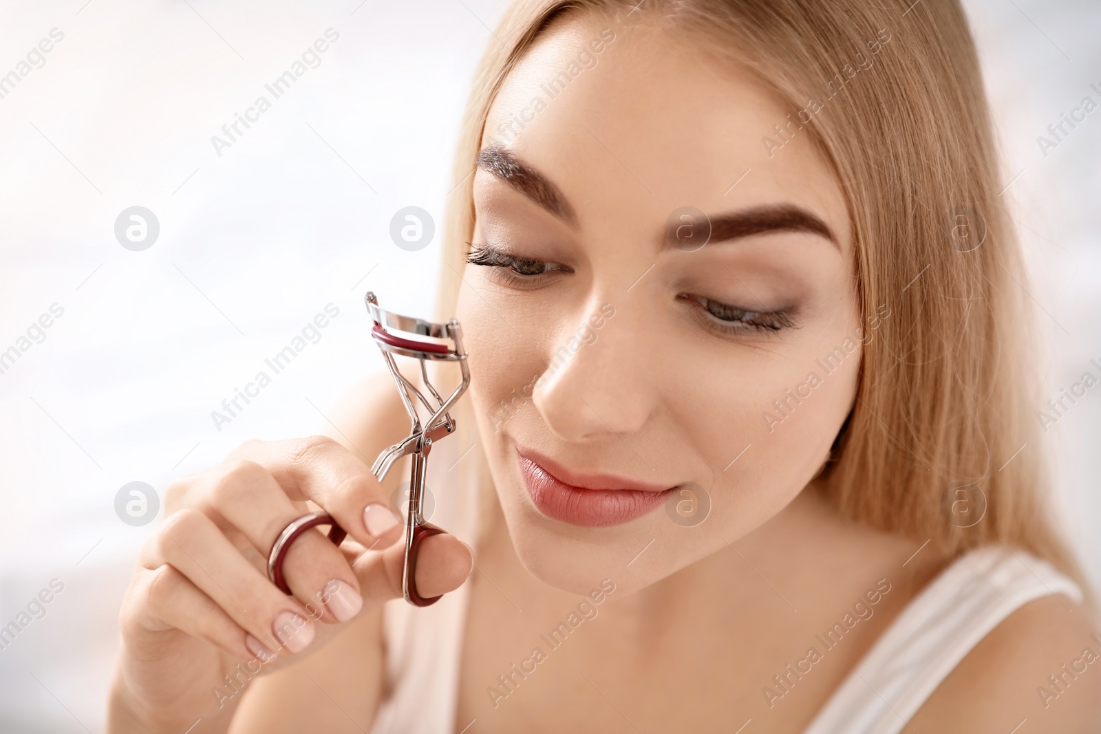 Photo of Young woman curling her eyelashes at home