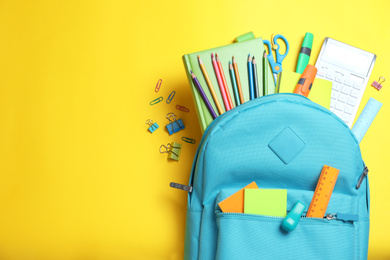Photo of Stylish backpack with different school stationery on yellow background, flat lay