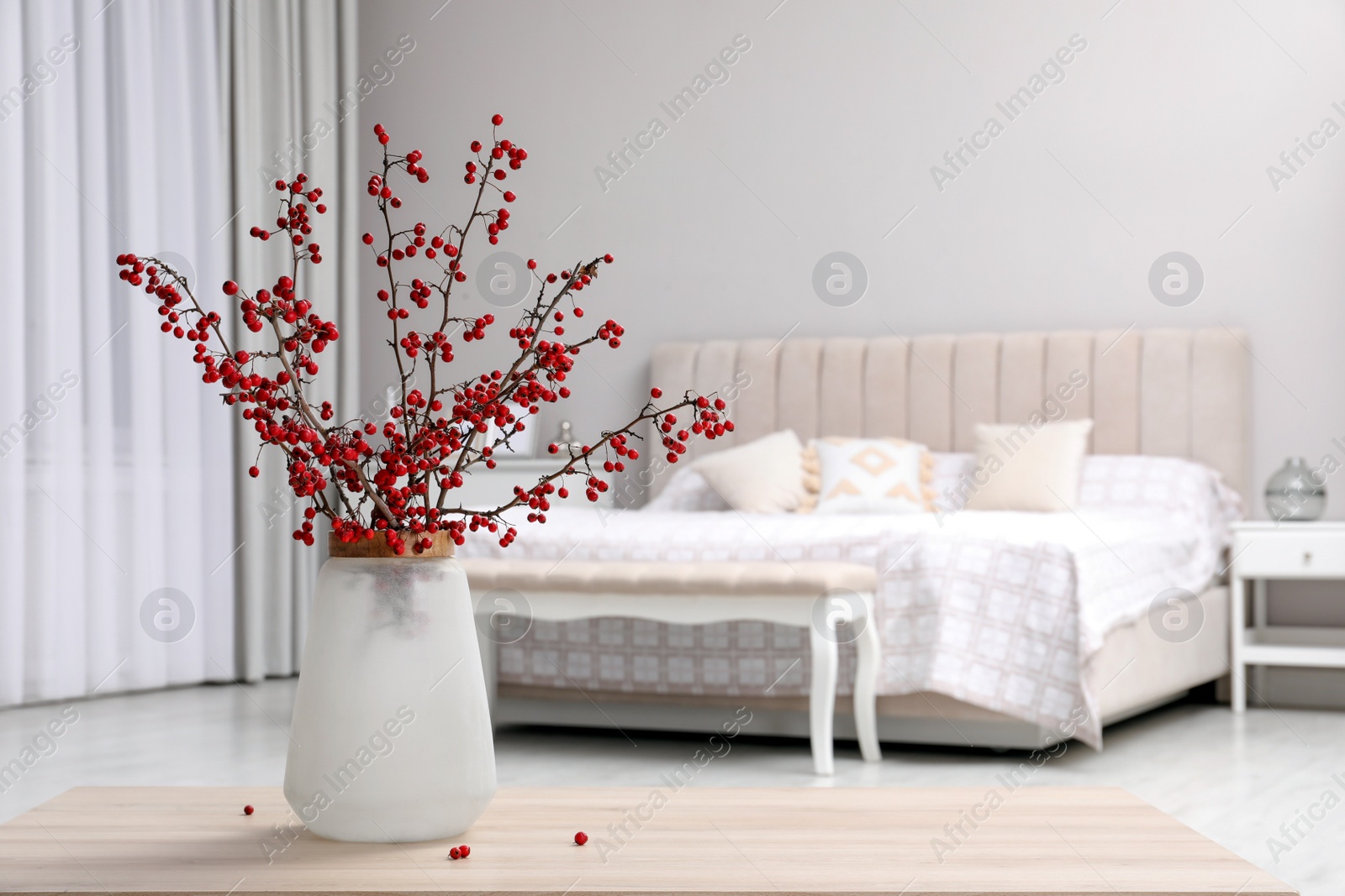 Photo of Hawthorn branches with red berries on wooden table in bedroom, space for text