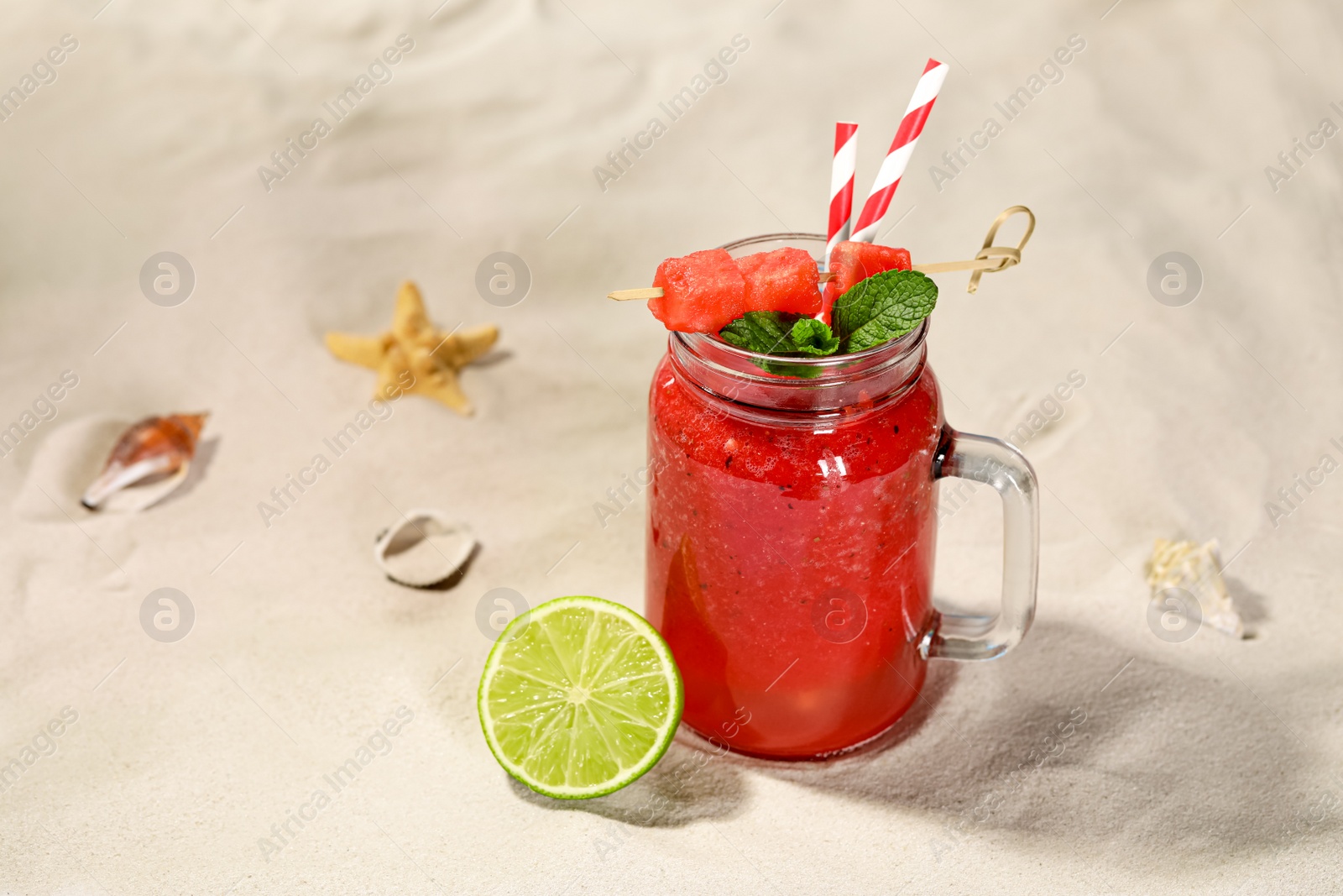 Photo of Tasty watermelon drink with lime in mason jar on sand, space for text