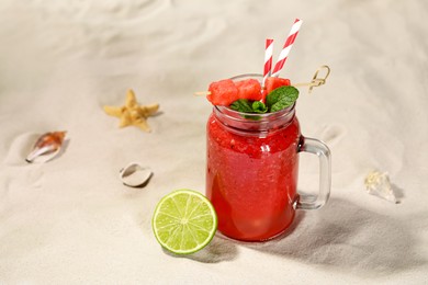Photo of Tasty watermelon drink with lime in mason jar on sand, space for text