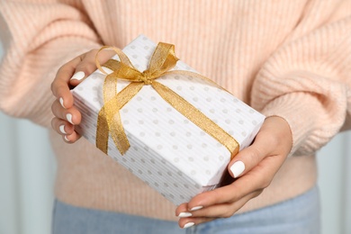 Woman in warm sweater holding Christmas gift on light background, closeup