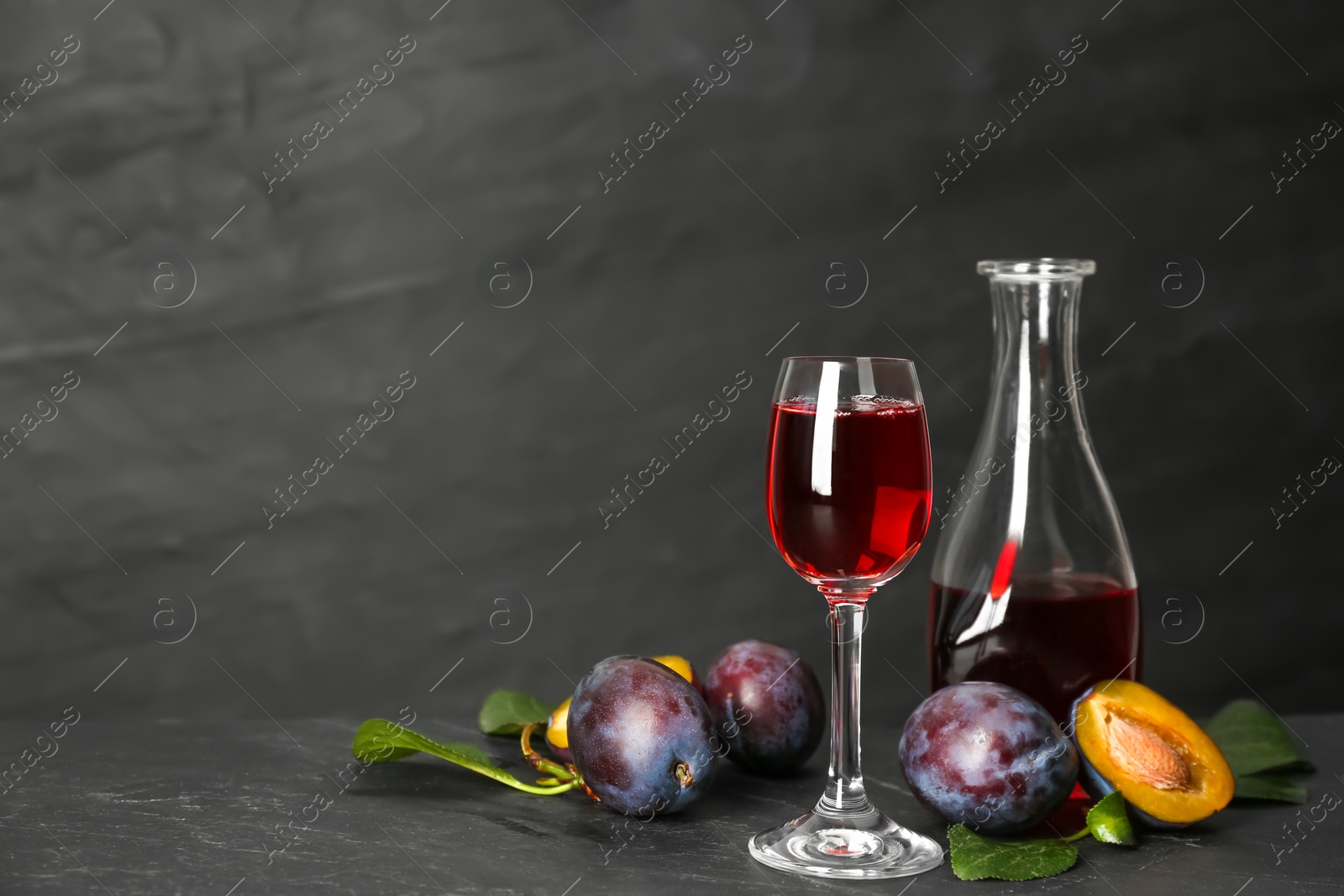 Photo of Delicious plum liquor and ripe fruits on black table. Homemade strong alcoholic beverage