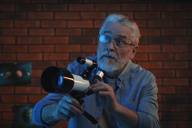 Senior man using telescope to look at stars in room