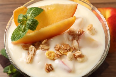 Photo of Tasty peach yogurt with granola, mint and pieces of fruit in dessert bowl on table, closeup