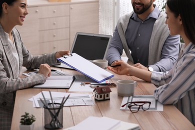 Happy young couple signing purchase contract in real estate agent's office, closeup. Mortgage concept