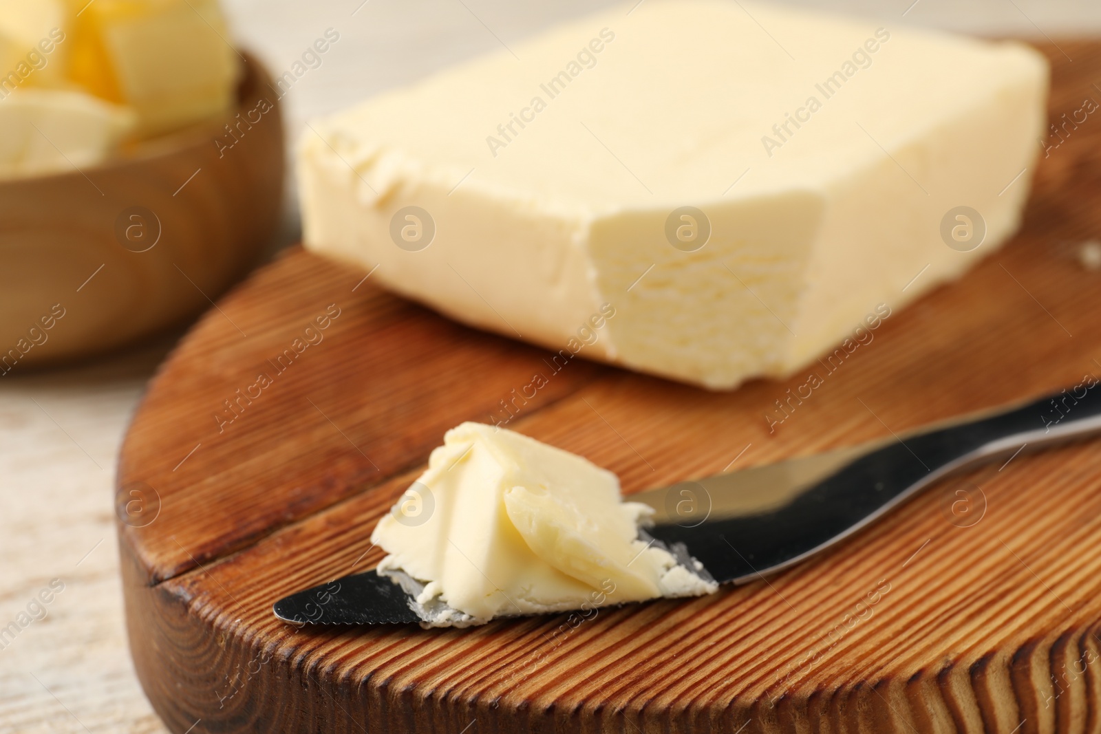 Photo of Tasty butter and knife on light wooden table, closeup