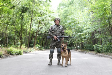 Photo of Man in military uniform with German shepherd dog, outdoors