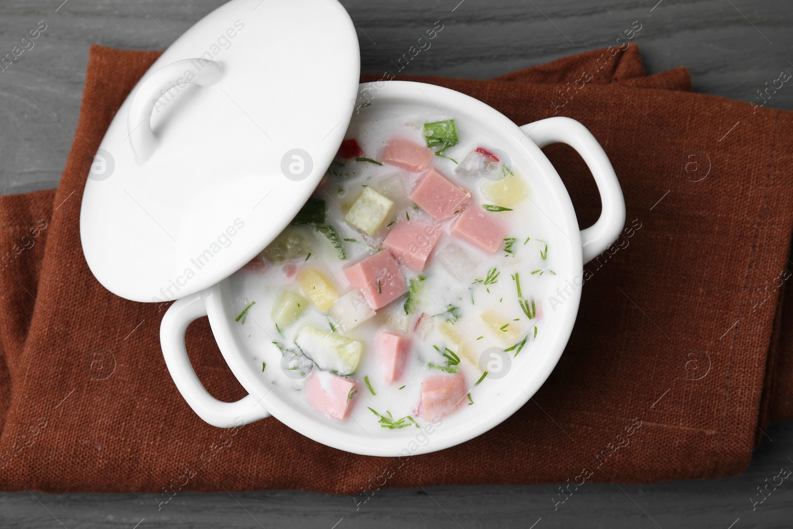 Photo of Delicious cold summer soup (okroshka) with boiled sausage in pot on grey wooden table, top view