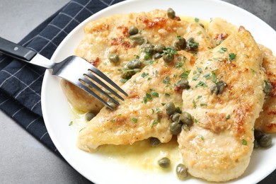 Photo of Delicious chicken piccata with herbs served on grey table, closeup