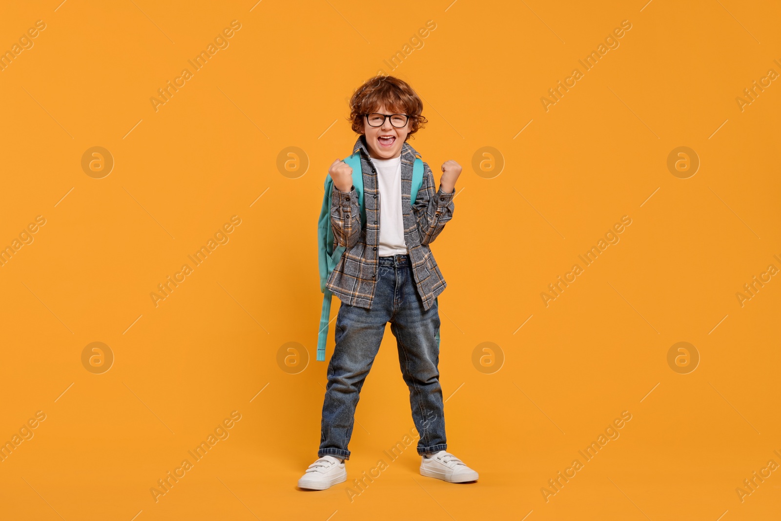 Photo of Emotional schoolboy with backpack on orange background