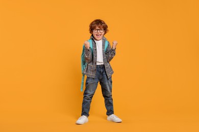 Emotional schoolboy with backpack on orange background