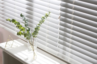 Photo of Vase with fresh eucalyptus branches on window sill in room. Interior design