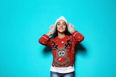 Young woman in Christmas sweater and knitted hat on color background