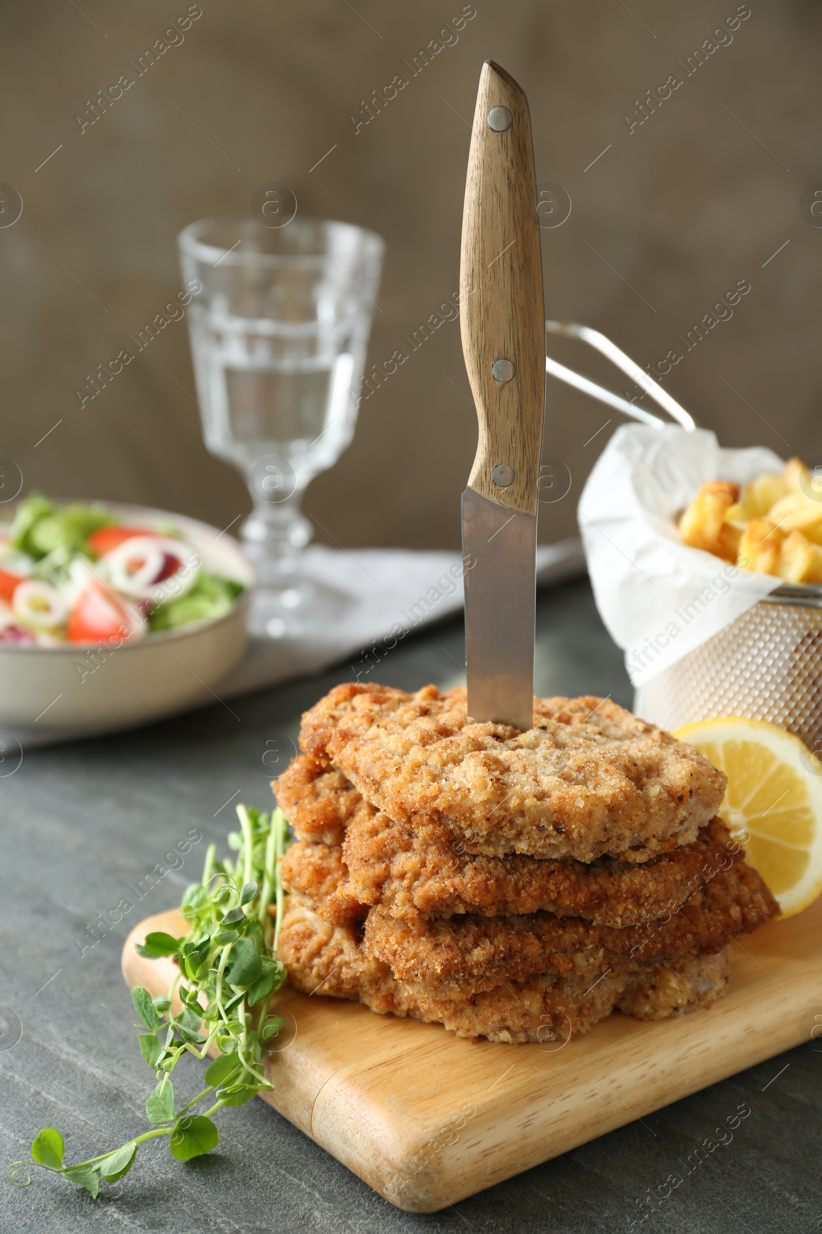 Photo of Tasty schnitzels served with knife and french fries on grey table