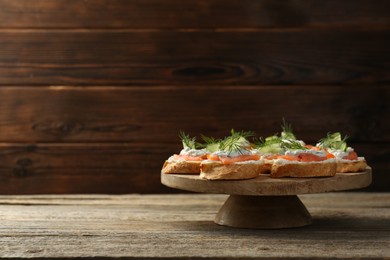 Tasty canapes with salmon, cucumber, cream cheese and dill on wooden table, space for text