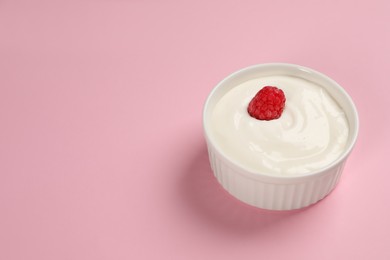 Tasty yogurt with raspberry in bowl on pink background, space for text