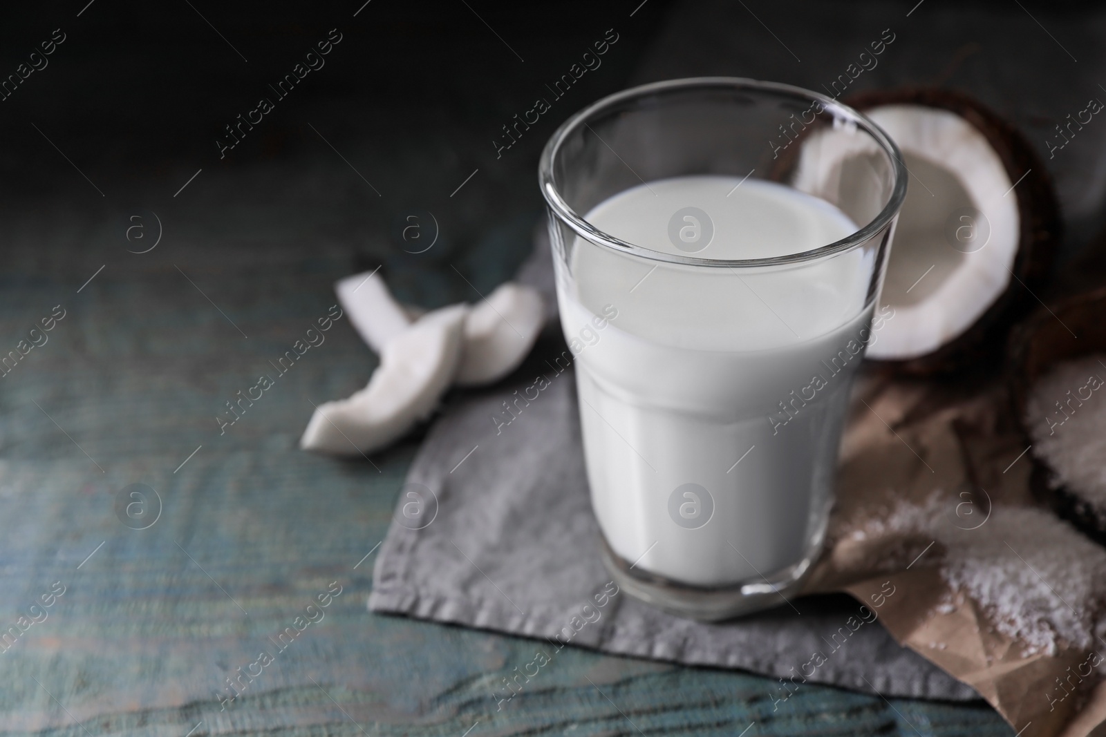Photo of Glass of coconut milk, flakes and nut pieces on wooden table, closeup. Space for text