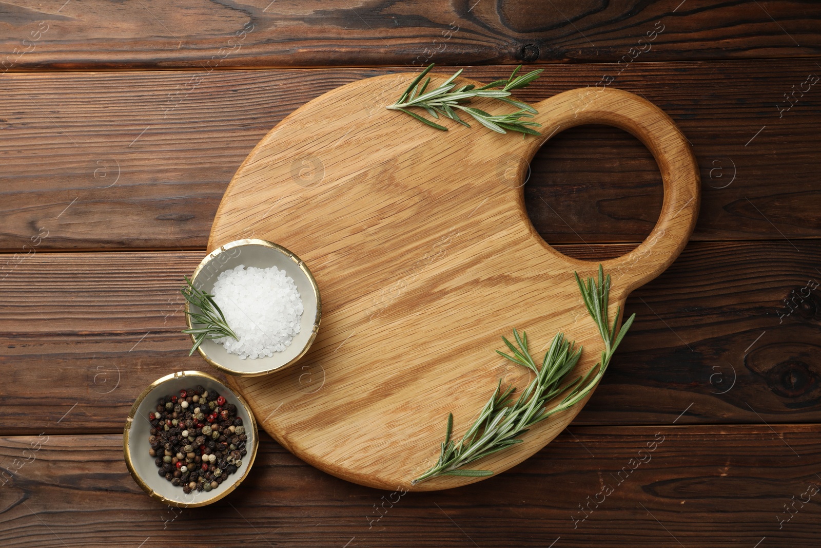 Photo of Cutting board, salt, pepper and rosemary on wooden table, flat lay. Space for text