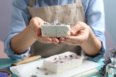 Photo of Woman holding hand made soap bar with lavender flowers at light blue wooden table, closeup