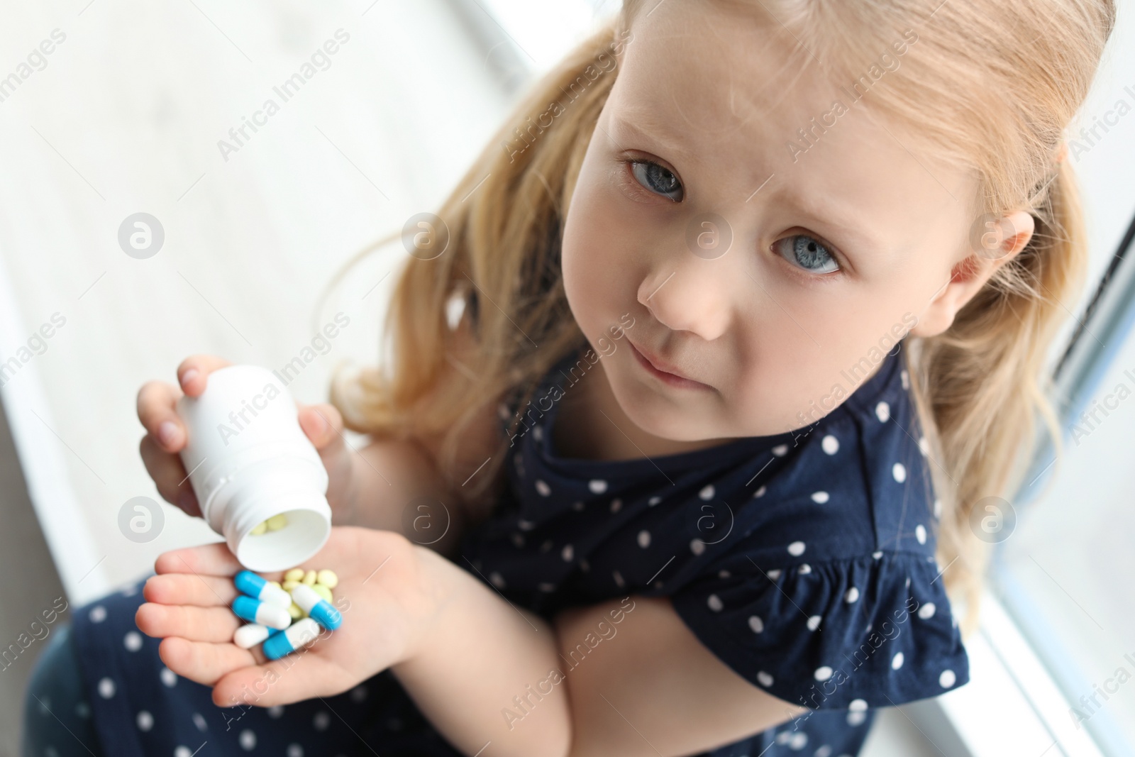 Photo of Little child with pills indoors, above view. Danger of medicament intoxication