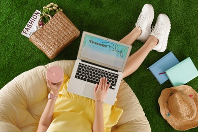 Woman and laptop with travel blogger site on artificial grass, top view