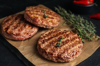 Tasty grilled hamburger patties with thyme on black table, closeup