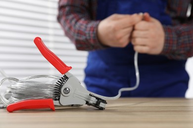 Photo of Professional electrician stripping wiring and cutter on wooden table indoors, selective focus