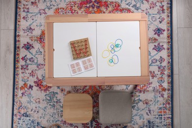 Photo of Wooden geoboard with letter W made of rubber bands and activity book on white table in room, top view. Motor skills development