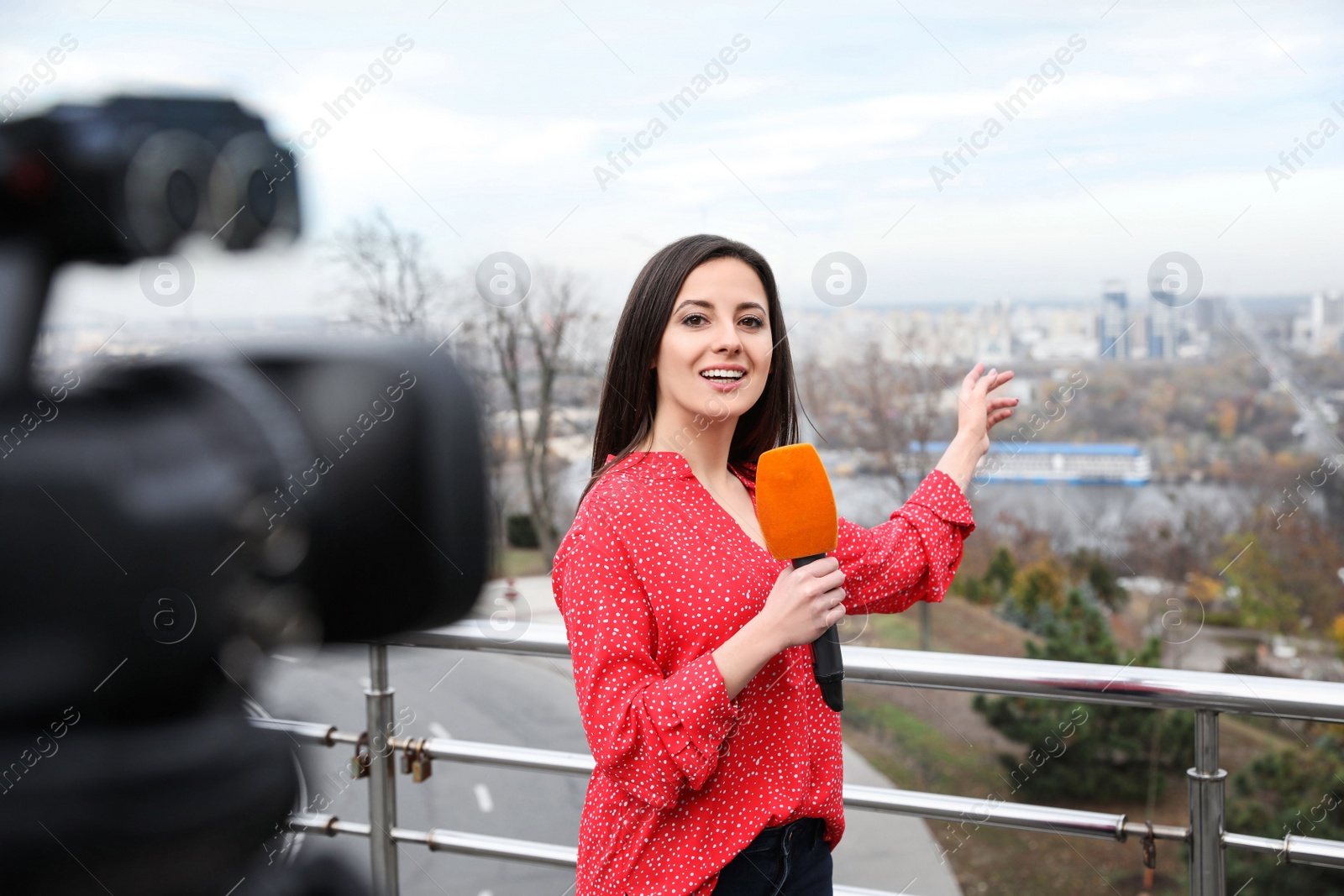 Photo of Young female journalist with microphone working on city street