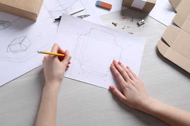 Photo of Woman creating packaging design at light wooden table, top view