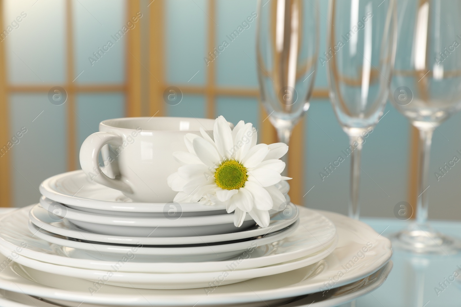 Photo of Set of clean dishware and flower on light blue table, closeup