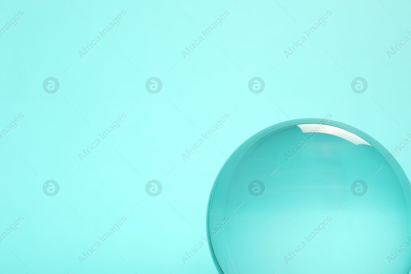 Photo of Transparent glass ball on turquoise background. Space for text