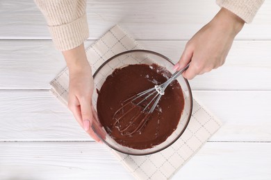 Photo of Woman mixing delicious chocolate cream with whisk at white wooden table, top view