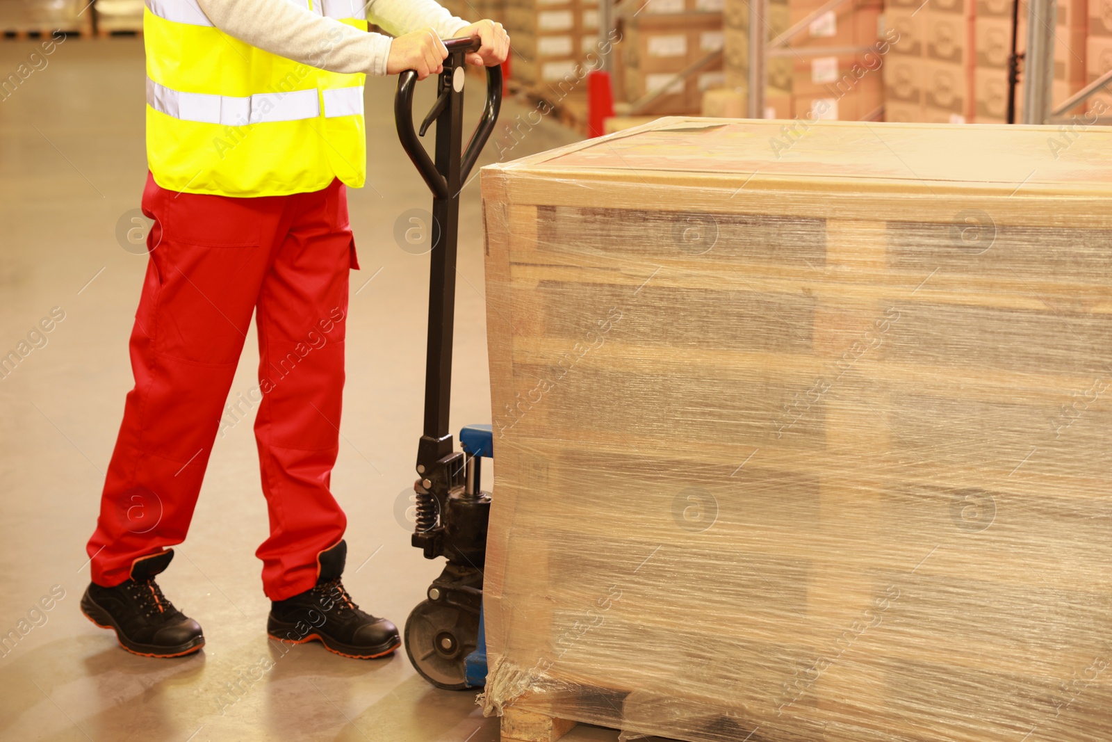 Image of Worker moving wrapped wooden pallets with manual forklift in warehouse, closeup