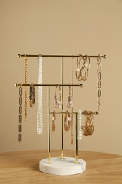 Holder with set of luxurious jewelry on wooden table near beige wall