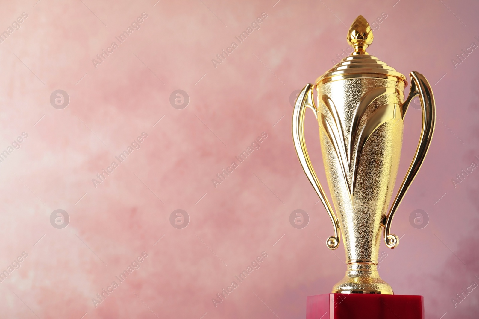 Photo of Golden trophy cup on pink background. Space for text