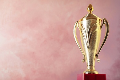 Photo of Golden trophy cup on pink background. Space for text