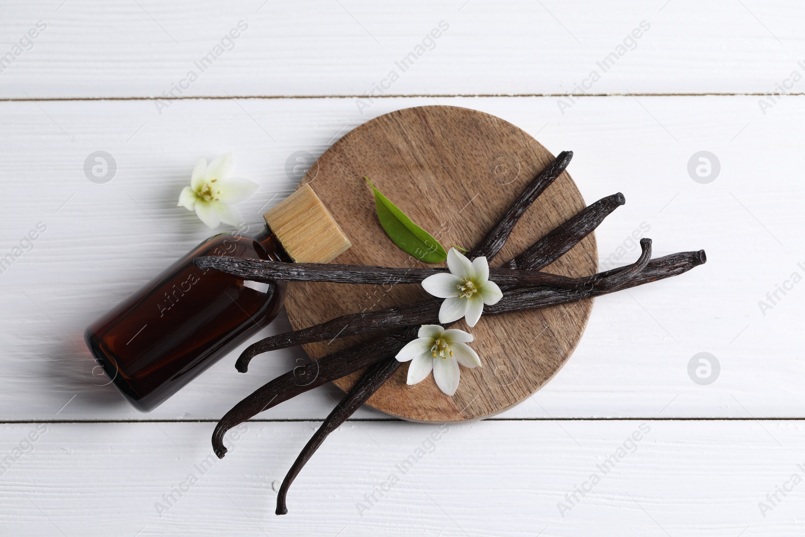 Photo of Vanilla pods, flowers, leaf and bottle with essential oil on white wooden table, flat lay