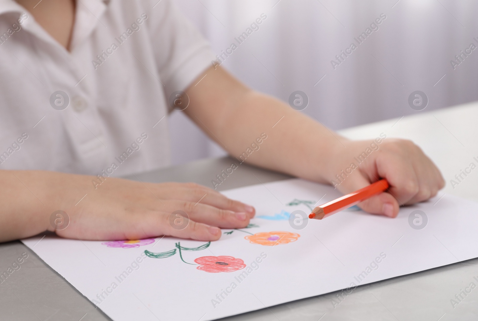Photo of Little boy drawing flowers with pencil at grey table indoors, closeup. Child`s art